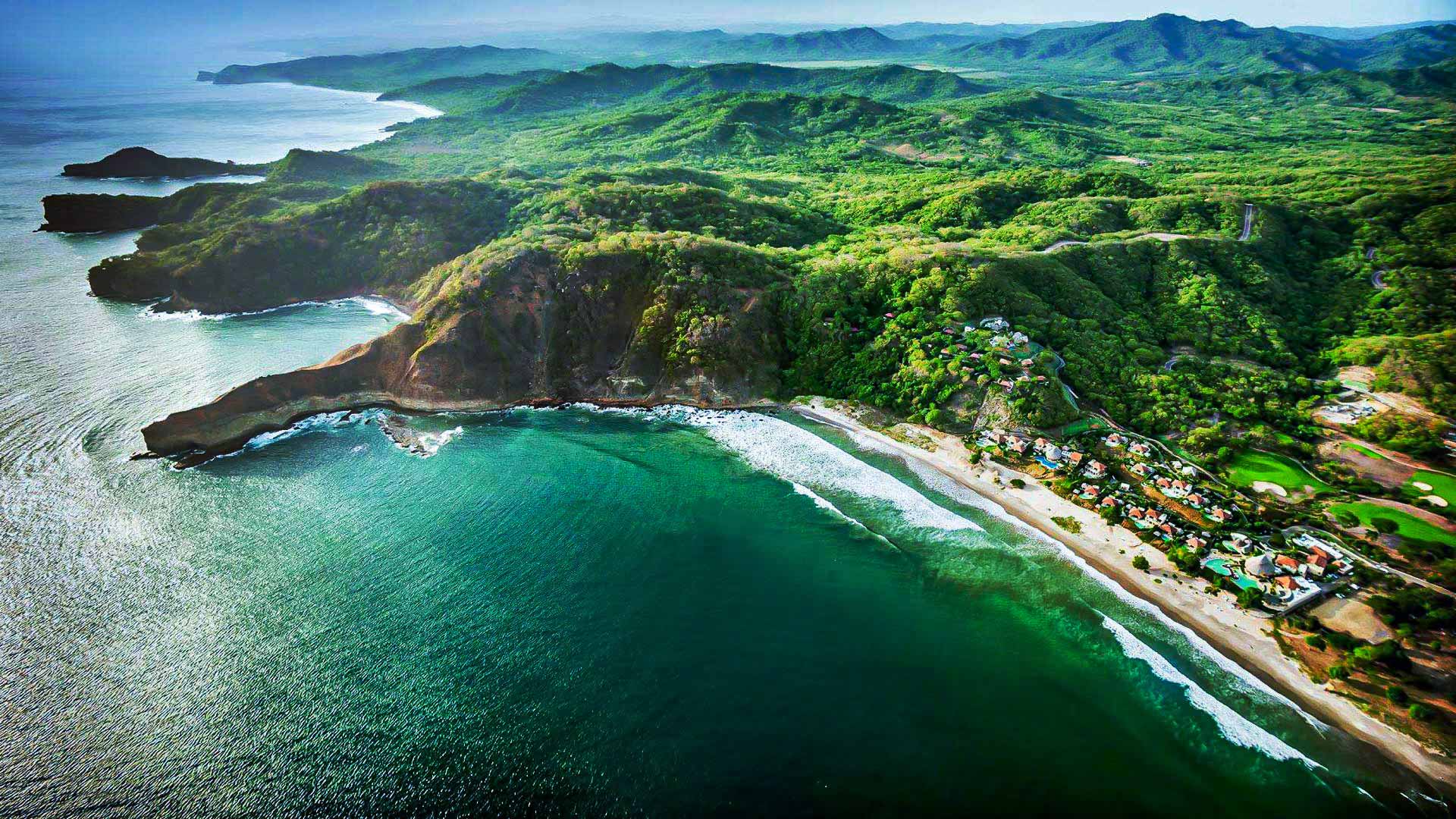 Aerial view of a Nicaragua Pacific coastline with a crescent beach, forested hills, and turquoise water