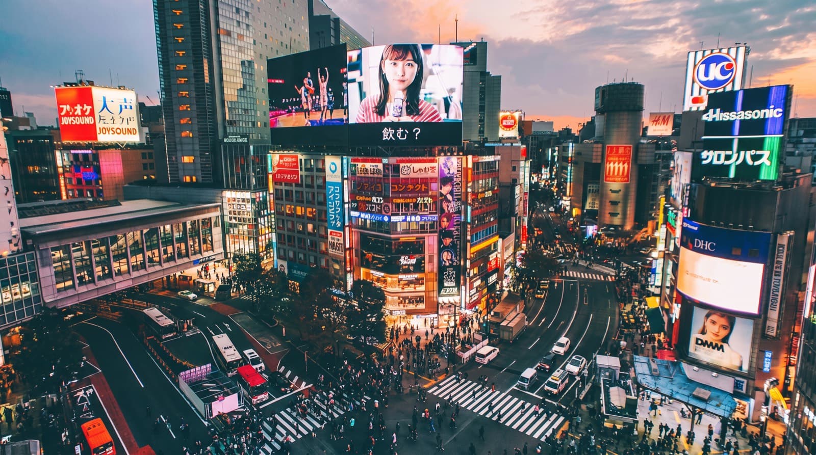Crowds crossing Shibuya Crossing in Tokyo at dusk under neon billboards